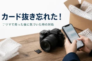 一眼レフとメモリーカード、段ボール箱の横でスマホからメッセージを送ろうとしている手元
